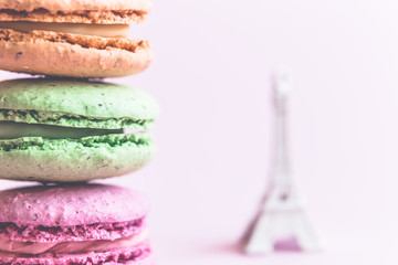Multicolored macaroon cookies and small Eiffel Tower isolated on rose background.