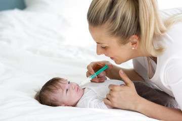 beautiful blond woman and mother, or doctor is feeding baby medicine with a medical syringe