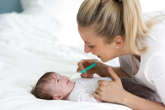 Beautiful Blond Woman And Mother, Or Doctor Is Feeding Baby Medicine With A Medical Syringe