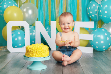 Portrait of cute adorable Caucasian baby boy in jeans pants celebrating his first birthday. Cake...