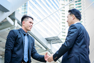 Fototapeta premium Two asian business have handshake with building and city background.