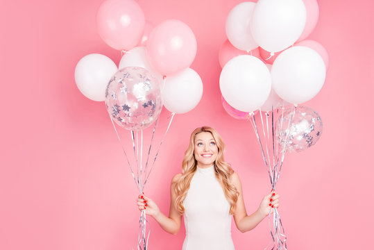 Portrait of trendy cheerful elegant girlfriend having many white air balloons in two hands looking up enjoying ballons isolated on pink background