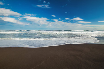 Halaktyr beach. Kamchatka. Russian federation. Dark almost black color sand beach of Pacific ocean. Stone mountains and yellow grass are on a background. Light blue sky