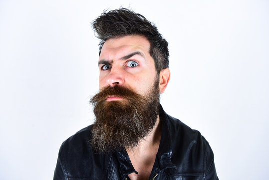 Hipster looks surprised and suspicious while raising his eyebrow. Masculinity concept. Man with beard and mustache on strict face looking at camera. Macho wears leather jacket, white background.