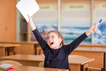 Happy child sits at the Desk in the classroom and enjoys the beginning of school holidays