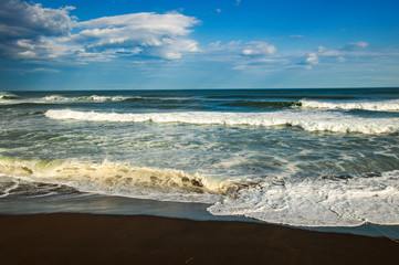 Halaktyr beach. Kamchatka. Russian federation. Dark almost black color sand beach of Pacific ocean. Stone mountains and yellow grass are on a background. Light blue sky
