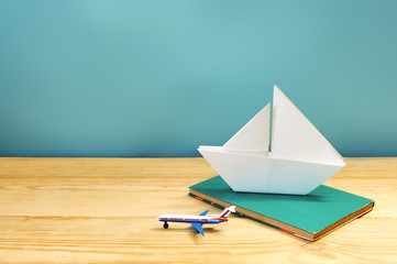 white paper ship, toy plane and book on wooden background