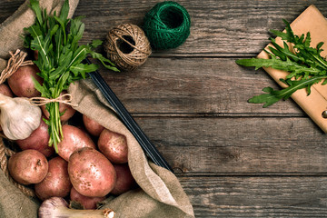 Raw whole washed organic potatoes, garlic and ruccola on sackcloth over old wooden plank background. Top view with space. Close up