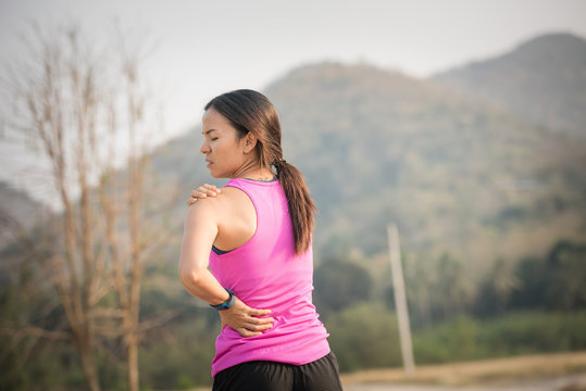 Neck pain during training. Athlete running woman runner with sport injury rubbing and touching upper back muscles outside after exercise workout in summer.