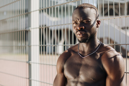 Seductive African American man with muscels poses with naked chest before the fence