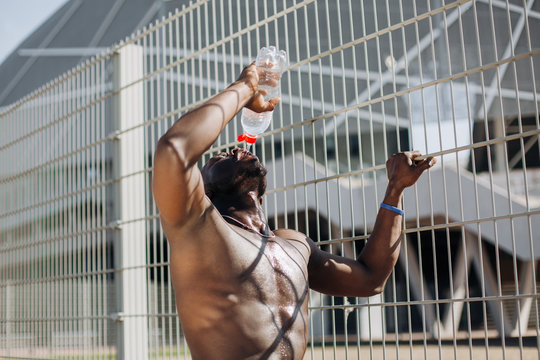 Seductive African American man with muscels poses with naked chest before the fence