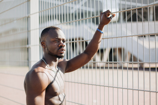 Handsome African American man with naked chest poses  before the fence in the morning