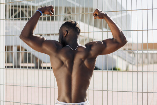 Seductive African American man with muscels poses with naked chest before the fence