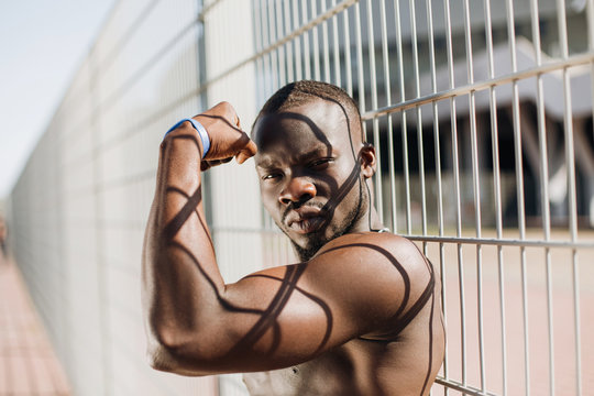 Seductive African American man with muscels poses with naked chest before the fence