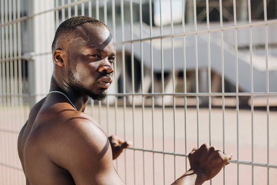 Seductive African American man with muscels poses with naked chest before the fence