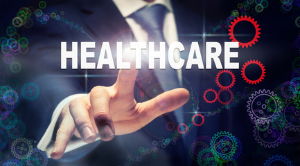 A businessman pressing a Healthcare business concept on a graphical display of cogs