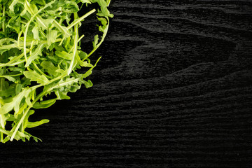 Fresh arugula flatlay isolated on black wood background.