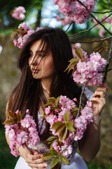 Fototapeta premium Wind blows brunette woman's hair while she poses before a blooming sakura tree