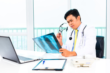 Fototapeta na wymiar Asian doctor diagnosis X-ray photograph in his medical office wearing stethoscope