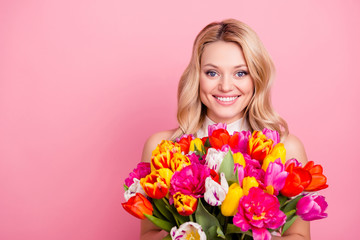 Portrait with copyspace, empty place of pretty wife, charming mother, cheerful positive woman holding big bouquet of colorful tulips in hands isolated on pink background looking at camera