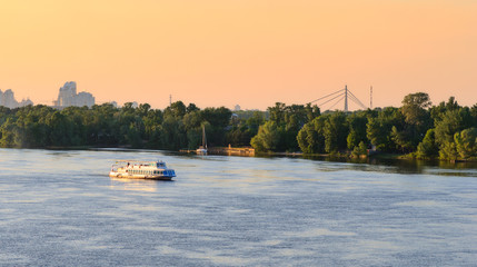 Obraz premium Kiev skyline with cruise tourist boat moving on Dnieper river in sunset colors