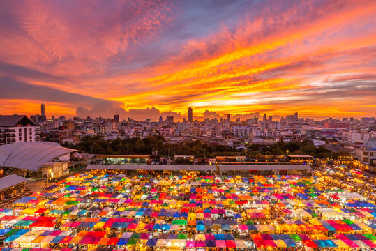 Top view of outdoor night market with Bangkok cityscape i n background under twilight evening sky and night light in Bangkok, Thailand
