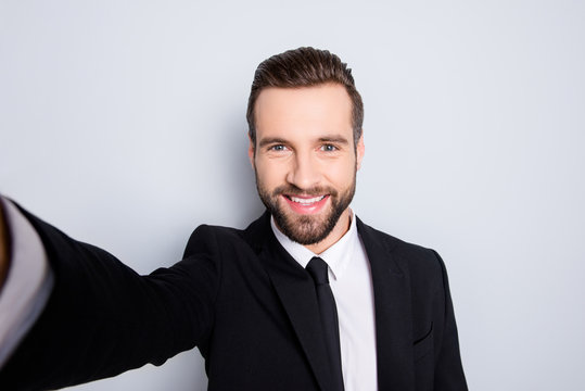 Self portrait of creative trendy man shooting selfie on smart phone with arm, looking at camera, isolated on grey background, having video-chat with partners friends
