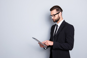Portrait with copyspace, empty space of busy smart man with modern hairstyle, stubble, having tablet in hands, checking email, chatting with partners over grey background