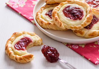 Danish pastries for breakfast on a wooden table. Pastries are stuffed with cheese cream and cranberries jam.