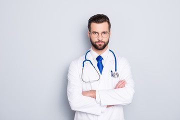 Portrait of attractive stylish doc with stubble in white lab coat, tie and stethoscope on his neck, having his arms crossed, looking at camera, isolated on grey background