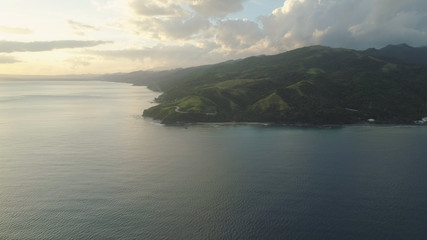 Fototapeta premium Aerial view of seashore with beach and mountains with sky and clouds at sunset. Philippines, Luzon. View of the ocean with the coastline. Tropical landscape in Asia.