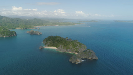 Aerial view of Groups islands with sand beach and turquoise water in blue lagoon among coral reefs, Caramoan Islands, Philippines. Mountains covered with tropical forest.