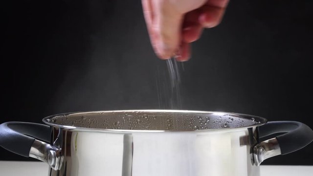 The man salt the soup. The pan is on the stove. Prepares the soup. Steam comes from the pan. 4k