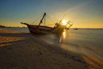 The beautiful golden lighting of fishing boat aground on the beach near the city.