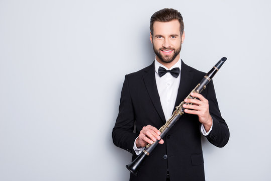 Portrait with copyspace, empty place of stylish cheerful man with hairstyle in black tux holding bassoon in hands, looking ta camera, isolated on grey background