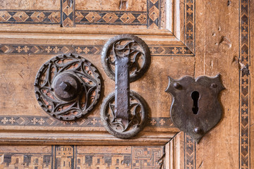 Foreground of old wooden door with iron handle. Old rusty gate handle on wooden door.
