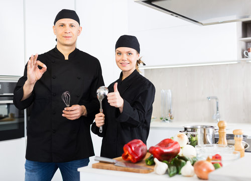 Man and woman young cooks in uniform showing thumbs up