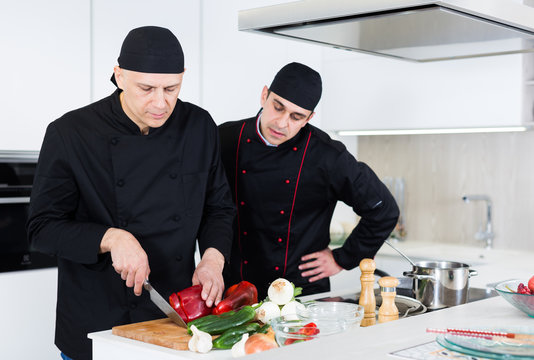 Two male cooks are making salad on their work place in the kitchen