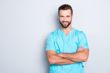 Portrait with copyspace, empty place of  joyful cheerful man with stubble in blue lab uniform, having his arms crossed, looking at camera isolated on grey background