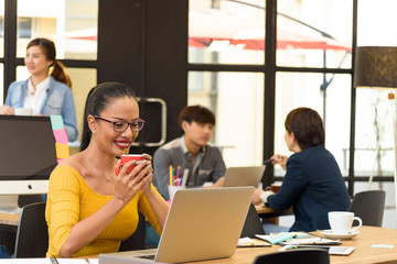 Asian charming beautiful business woman drink coffee between working in modern office and blurred multi ethnic business person group in casual suit in background. Project and Business concept.
