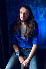 man with long hair and beard sits at home on a chair by the window