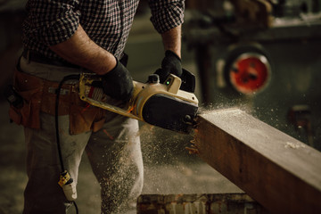 carpenter in the workshop saw a piece of wood with an electric chainsaw