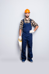 Full size body portrait of attractive handsome master with stubble, looking at camera holding hand on waist having saw in arm, isolated on grey background