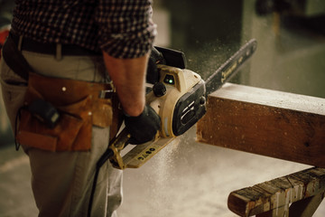 carpenter in the workshop saw a piece of wood with an electric chainsaw