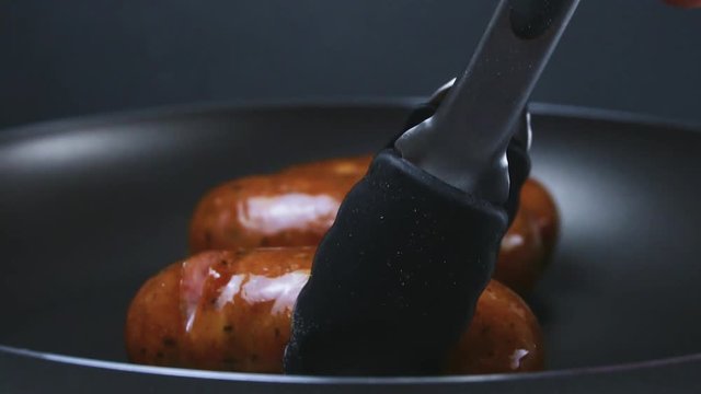 German sausages are fried in a frying pan. Sausages turn with forceps. Slow motion.