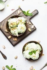 Pistachio ice cream with nuts, decorated with mint leaves in brown bowls, light background, top view