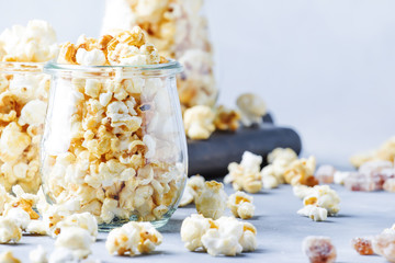 Caramel sweet popcorn in glass jars, gray background, selective focus