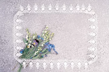 Velvet curtains Pansies lily of the valley, pansies and forget me not bouquet laying on an silver background in the lace frame with copy space for your greeting or invitation text. Holiday card.
