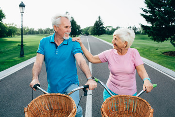 Senior couple with their bicycle, smiling at each other, while standing at city park