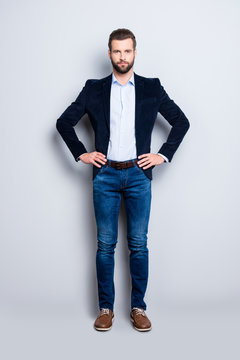 Full size body portrait of elegant attractive teacher with stubble holding two arms on waist looking at camera isolated on grey background, wearing jacket jeans shirt